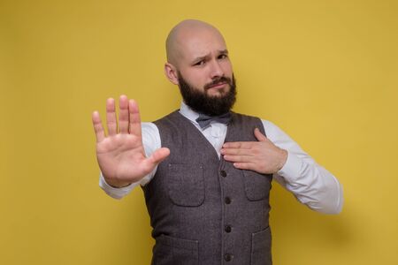 Mature man making stop sign on yellow studio wall.