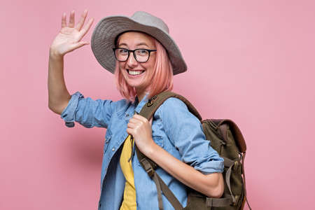 Happy caucasian woman in summer hat wearing backpack waving saying helloの写真素材