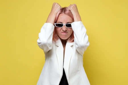 Frustrated and stressed young businesswoman in white suit and sunglasses.