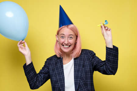 Beautiful young woman in party hat with air balloon on yellow backgroundの写真素材