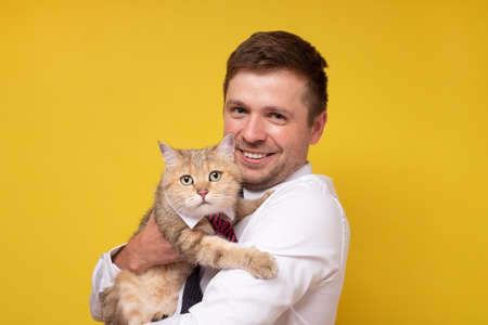 Caucasian young man with british tabby cat isolated on yellow background.