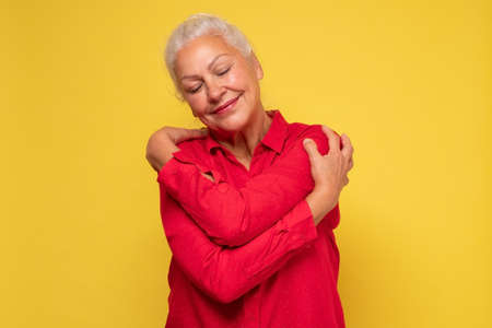 Woman wearing red clothes hugging herself being positive, smiling confident.の写真素材