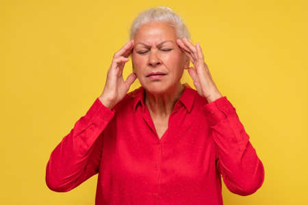 Elderly woman holding hands to her temples having terrible headache.の写真素材