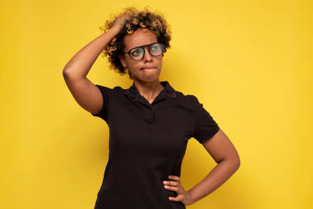 Young african woman in glasses scratching head, thinking daydreaming deeply about somethingの写真素材