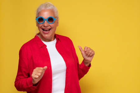 Cheerful old woman wearing trendy sunglasses, isolated on yellow background laughing.の写真素材
