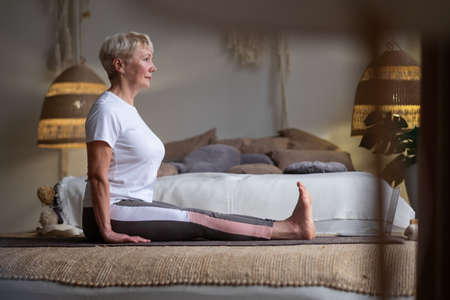 Senior woman practicing yoga, sitting in Dandasana exercise at homeの写真素材