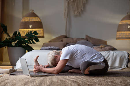 Senior woman practicing yoga concept, sitting in Janu Sirsasana exercise, Head to Knee Forward Bend poseの写真素材