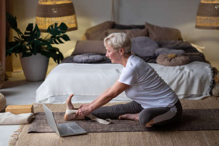 Senior woman practicing yoga concept, sitting in Janu Sirsasana exercise, Head to Knee Forward Bend poseの写真素材