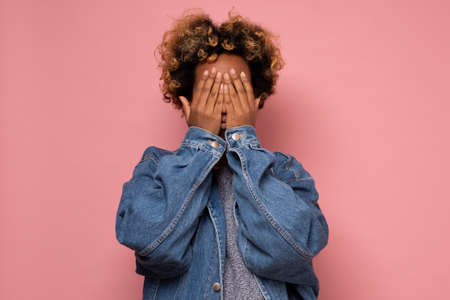 Young african woman covering face with hands hiding her emotions from everybody.の写真素材