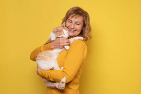 Caucasian woman lovingly hugging cat on yellow wall.の写真素材