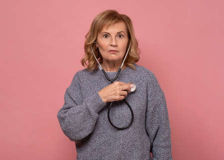 Young mature female woman looking surprised when checking her heart with stetoscope