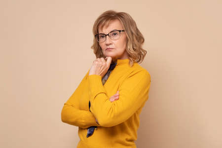 Serious caucasian woman in glasses standing with folded hands and looking at cameraの写真素材