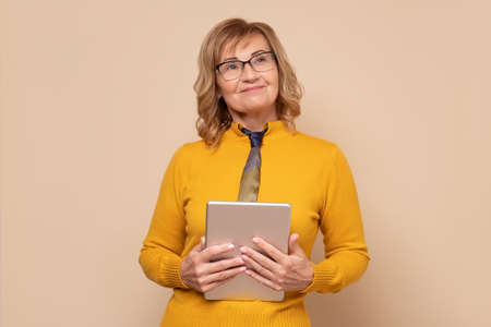 Mature woman in glasses holding tablet computer working on touching screen.の写真素材
