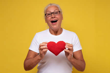 Senior hispanic woman with glasses smiling in love showing red heart.の写真素材