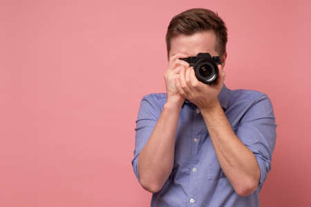 Traveler and photographer. Studio portrait of handsome young man holding photocamera taking photo. Yellow blackground.の写真素材