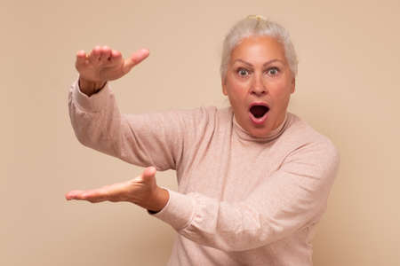 Amazed senior caucasian woman showing with hands large size feels shockedの写真素材