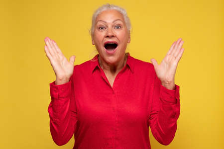 Surprised happy senior woman holding hands up being excited with newsの写真素材