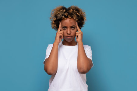 Serious african woman holding fingers on her temples with concentrated and focused expressionの写真素材