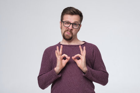 Young handsome man with glasses and beard smiling positive doing ok sign.