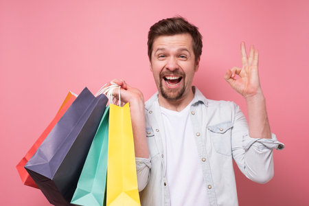 Happy caucasian young man with shopping bags approving ok gesture.の写真素材