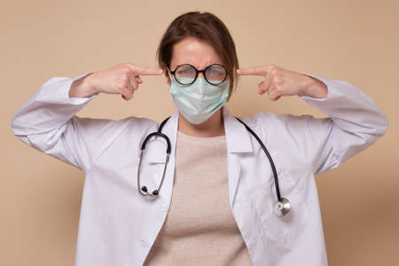 Irritated doctor woman in medical mask plugs ears, complains on noiseの写真素材