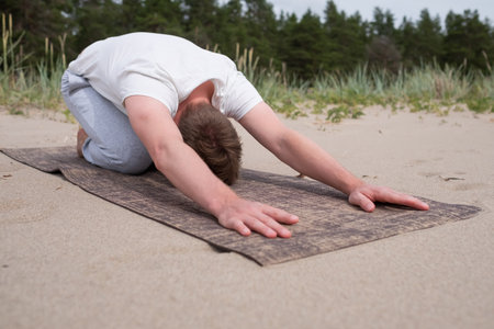 Man doing childs pose in yoga at the beachの写真素材