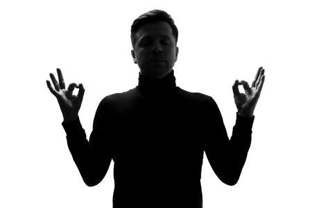 Silhouette of man with peaceful expression meditating, holding his hands in mudra gestureの写真素材
