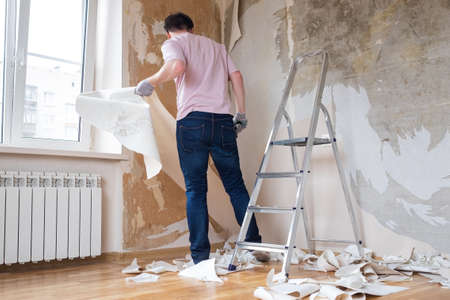 Caucasian man tearing off old wallpaper from wall preparing for home redecorationの写真素材