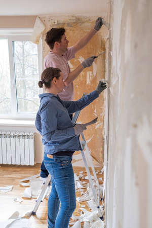 Young couple removing old wallpaper from walls preparing for flat renovation.の写真素材