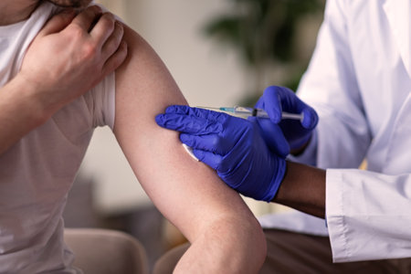 African doctor with syringe doing injection of vaccine to male patientの写真素材