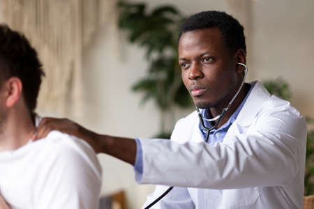 African doctor examining young male patient listening lungs and heart