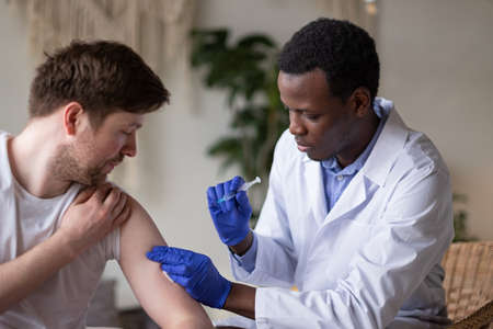 African doctor with syringe doing injection of vaccine to male patientの写真素材