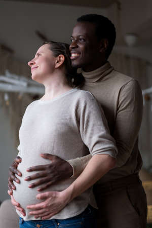 Black expectant father holding hands on belly of his caucasian pregnant wife. Mixed marriage.の写真素材