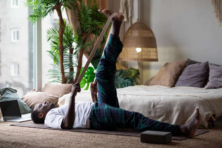 Young sporty african man working out at home , warming up using yogic belt