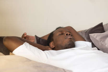 Handsome ethnic black african man resting in bed sleeping or napping.