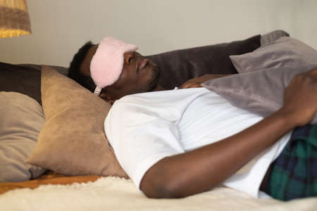 Handsome ethnic black african man resting in bed sleeping or napping.