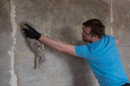 Caucasian man washing walls from dust using old ragの写真素材