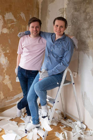 Couple smiling at camera standing near wall redecorating their new flatの写真素材
