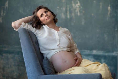 Pregnant caucasian woman posing in sofa during photoshoot.