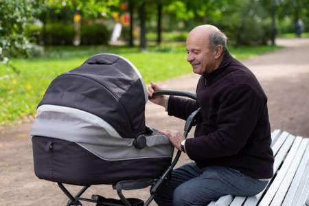 Grandfather pushing newborn in stroller in parkの写真素材