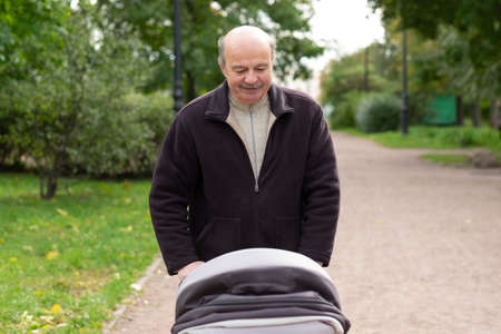 Grandfather pushing newborn in stroller in parkの写真素材