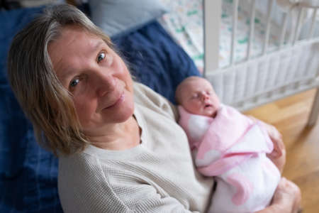 Elderly woman grandmother holding a newborn in her arms