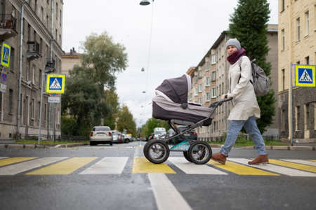 Woman with stroller on crosswalk crossing the road looking aside checking cars.