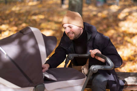 Happy young father with pram sitting on bench in nature at parkの写真素材