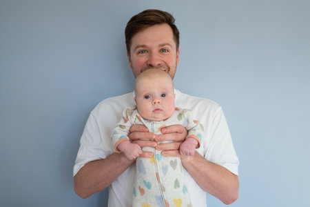 Young man holding a 3months old baby, isolated on blue background