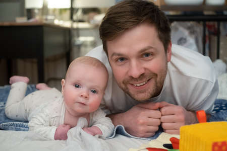 happy father and his adorable little daughter lying together on bed looking at camera.の写真素材