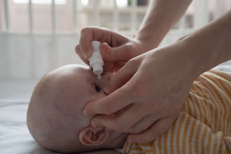 Mother is treating newborn eye inflammation by givining eye drops.の写真素材