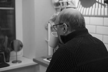 Senior man looking by window, holding cup of tea