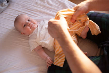 Caucasian parent changing and dressing up baby.