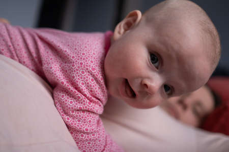 Baby girl looking at camera while lying on mom playingの写真素材